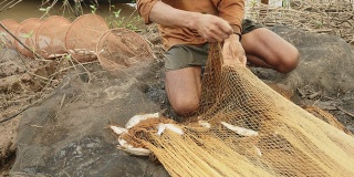 渔夫从他的渔网中取出被缠住的鱼，并把它放在河岸的网箱里
