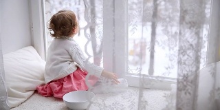 可爱的小女孩坐在窗台上。冬季。多莉。