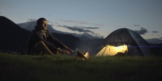 年轻人走进去，露营在户外的山在晚上用营火温暖他和走开-高清视频录像
