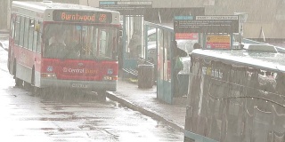 公交车站繁忙雨天雨天，车灯在雨淋的人等待