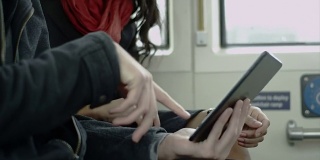 一对情侣在公交车上一起笑着玩平板电脑