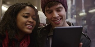 一对年轻夫妇在公交车上玩着他们的数码平板电脑玩得很开心