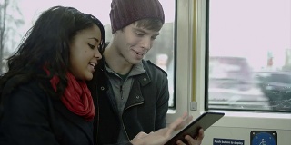 一对夫妇在公交车上玩着他们的平板电脑玩得很开心