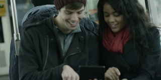 一对夫妇坐在公交车上玩着他们的平板电脑玩得很开心