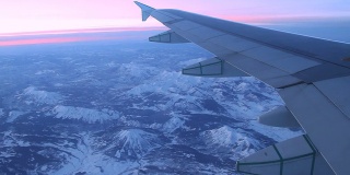 日出日落时，飞机飞过多雪的岩石山脉