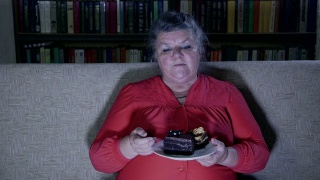 胖老女人一边看电视一边吃蛋糕视频素材模板下载