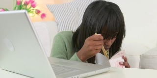 黑人妇女一边用笔记本电脑一边吃中餐外卖