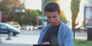 年轻男性在户外的相机前微笑着浏览平板电脑
