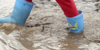孩子脚穿胶靴走在泥坑里，工地上