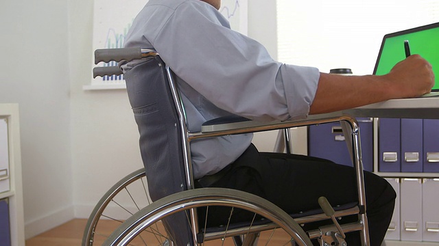 坐在轮椅上使用绿屏笔记本电脑的残疾商人