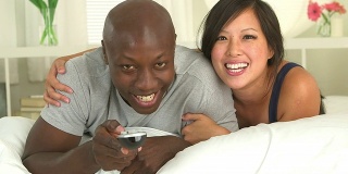 黑人和亚洲夫妇一起在床上看电视