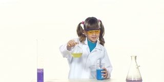扎着马尾辫，戴着防护眼镜的小女孩正在做化学实验——混合，站在桌子旁边，孤立在白色的背景上