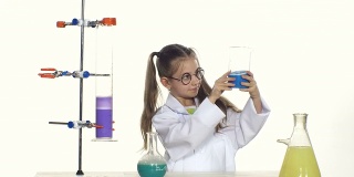 可爱的女孩马尾辫在统一和圆形眼镜评估两种液体，站在桌子旁边的化学实验的白色背景