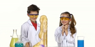 两个美丽，可爱的化学家孩子做有趣和成功的实验孤立在白色背景，慢动作