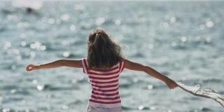慢动作:拿着丝巾在海边迎着风的女孩