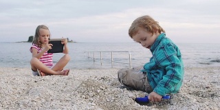 慢动作:男孩在沙滩上玩，女孩用触控板拍照