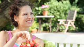 坐在长凳上吃草莓的女人。视频素材模板下载