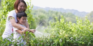 亚洲母亲和儿子正在浇树