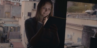 一个女人坐在窗台上用着平板电脑
