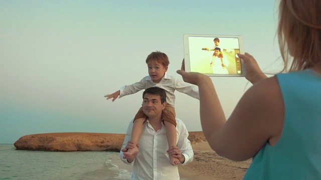 母亲与pad射击父亲和儿子在海滩上