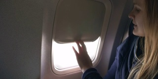 在飞机上用平板电脑合上百叶窗的女人
