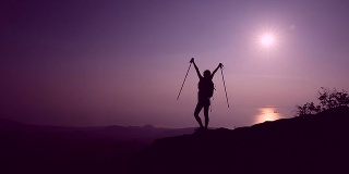 欢呼的女徒步者在日落山顶张开双臂