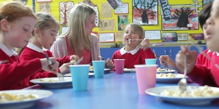 老师坐在餐桌旁吃午餐的学童