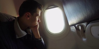 无聊的飞机乘客看着舷窗，飞机无聊。飞机高空载客，客机机翼涡轮和舷窗云雾，飞机内景拍摄，国际喷气飞行运输，白天的天空