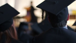 在大学毕业典礼上，兴奋的学生们戴着学士帽和学士服鼓掌视频素材模板下载