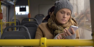年轻可悲的女人在公交车上用智能手机
