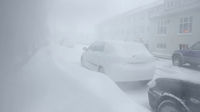 冰岛雷克雅未克，白雪覆盖的雪堆阻塞了居民区的人行道上的汽车