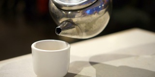 手将金属茶壶中的中国茶倒入瓷杯中