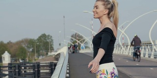 漂亮的金发女孩站在桥上向某人挥手。