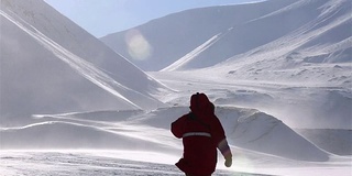 一个孤独的旅行者正穿过暴风雪，背景是雪山。