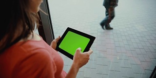 一个女人在窗前用平板电脑。绿屏