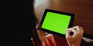 女性在餐桌上使用平板电脑。绿屏