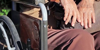 一位老年妇女手放在轮椅上。