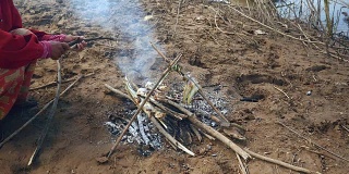 妇女在烤鱼下添加小树枝以保持炉火燃烧