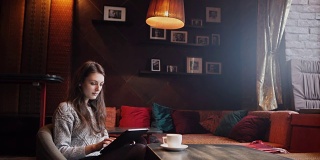 在咖啡店喝咖啡和使用平板电脑的年轻女子