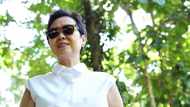 酷酷的亚洲资深女性戴太阳镜在绿色自然背景白色衬衫