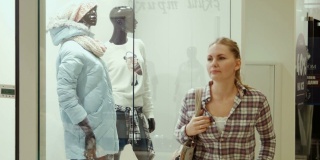 这个女孩在购物中心看一家服装店的橱窗