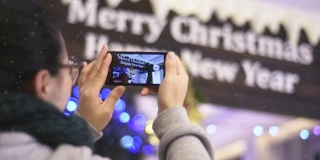 一个中国女孩在圣诞树下用手机拍照