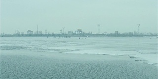 冬季垂钓者在冰上，背景是水力发电站