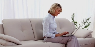 一个成熟的女人坐在沙发上用着笔记本电脑