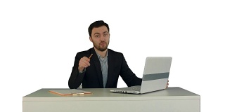 快乐的商人坐在办公室与笔记本电脑，说在摄像头上的白色背景孤立