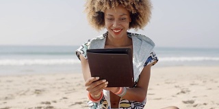非裔美国女孩在海滩上使用平板电脑