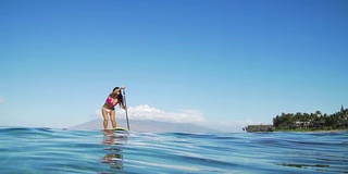 冲浪女孩站起来划桨在夏天的一天