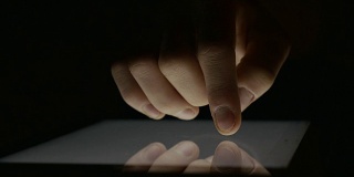 在黑暗中使用平板电脑的手的特写