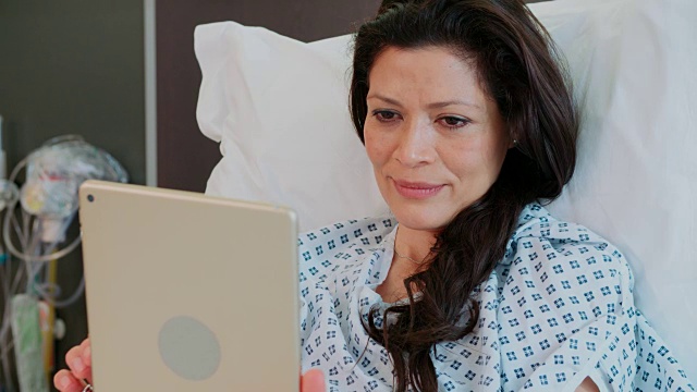 在医院病床上使用数字平板电脑的女性患者
