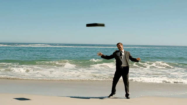 Happy businessman throwing his suitcase on the beach